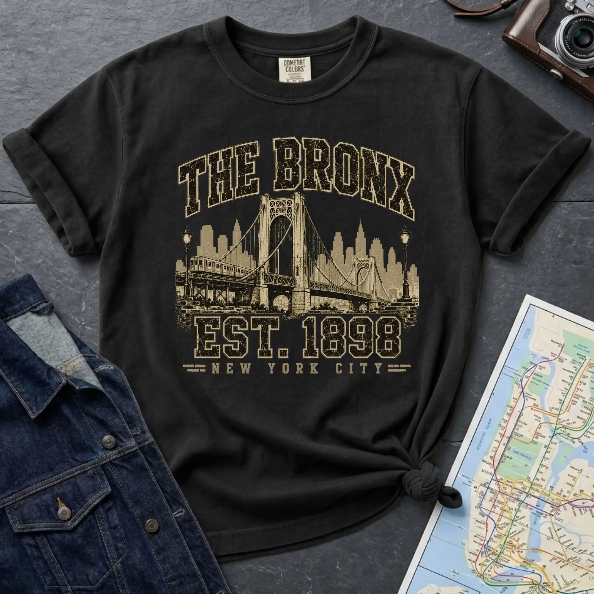 Black t-shirt with 'The Bronx Est. 1898' design on a dark surface with a map and denim jacket.