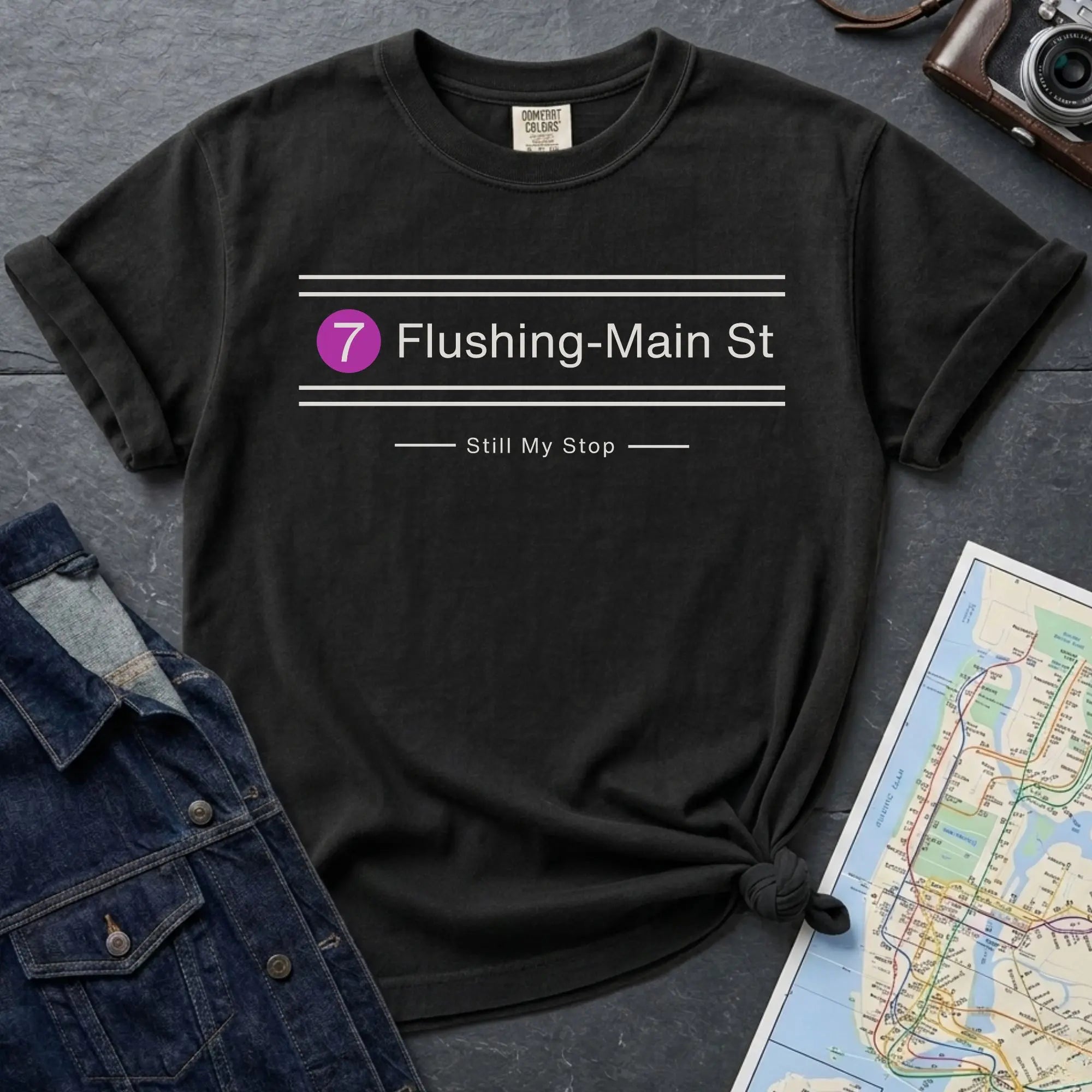 Black t-shirt with 'Flushing-Main St' design on a gray surface with a map and denim jacket.