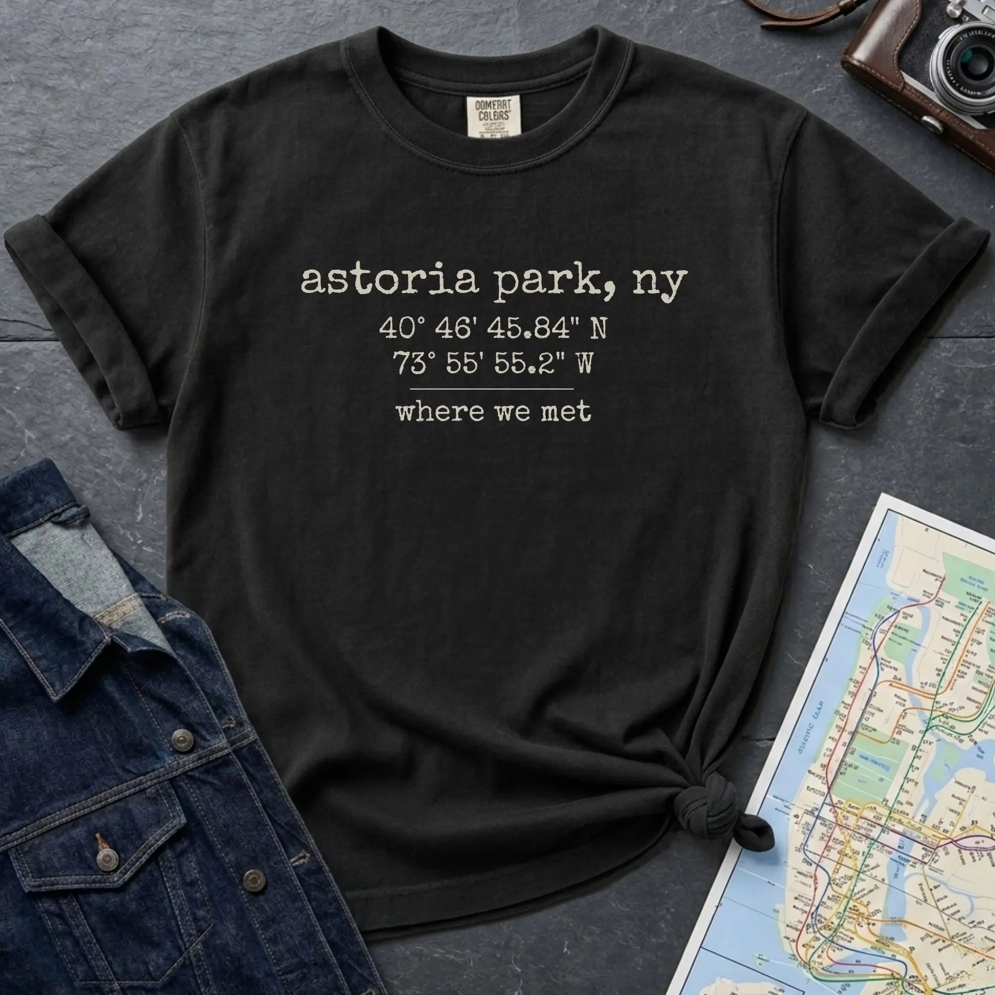 Black t-shirt with Astoria Park coordinates on a dark surface with a map and jacket.