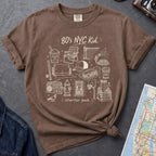 Brown Comfort Colors t-shirt with an 80’s NYC Kid starter pack graphic featuring Italian ice, stickball, a fire hydrant, corner coffee, and stoop illustrations.