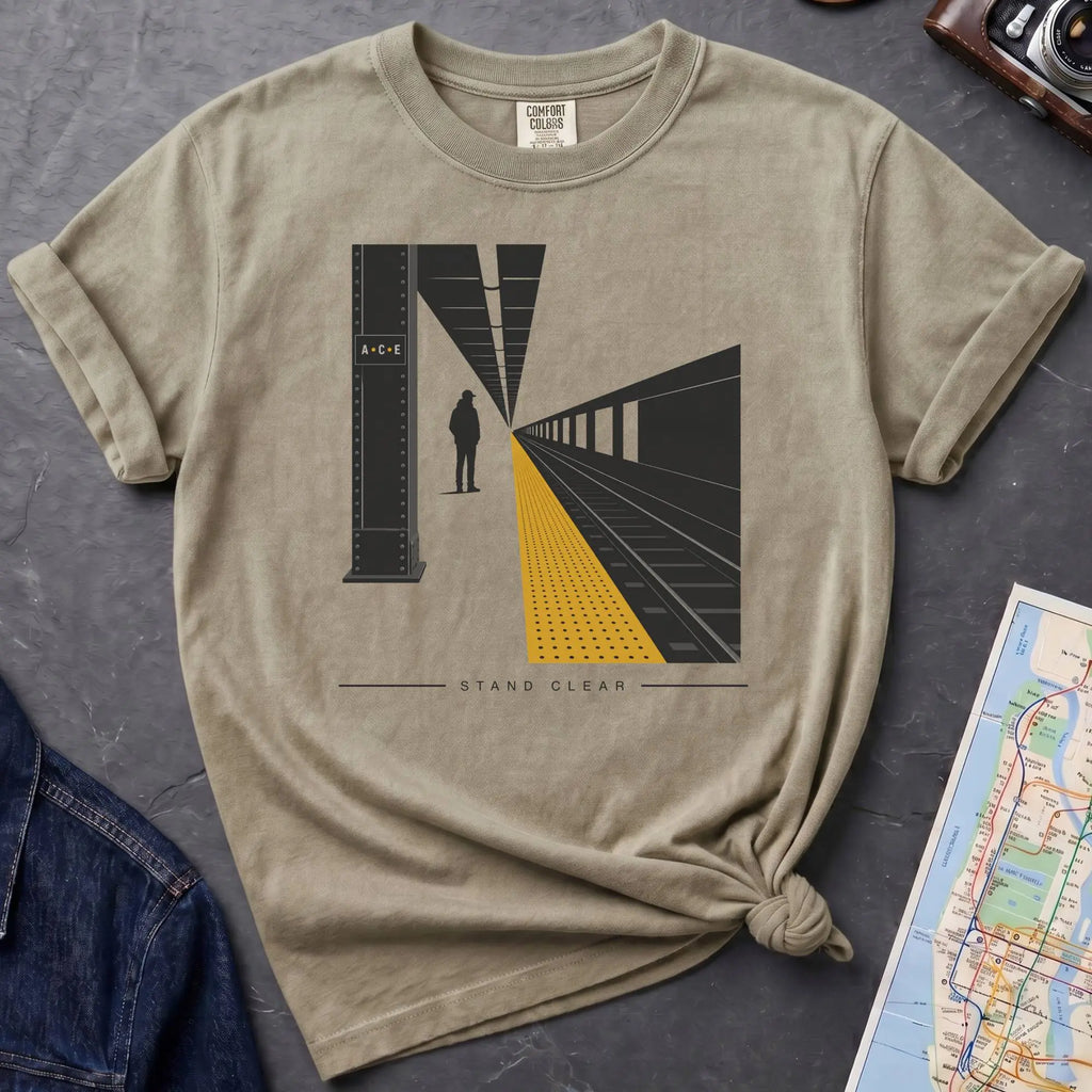 Khaki colored t-shirt with a graphic design of a train station platform, denim jacket, and map on a dark surface
