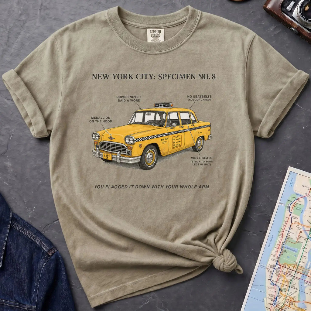 Khaki colored Comfort Colors t-shirt with yellow taxi graphic and text on a dark surface with denim jacket and map.