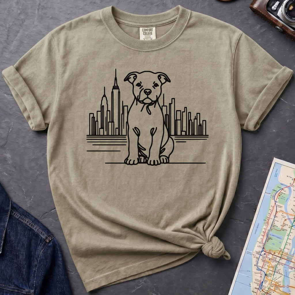 Khaki colored t-shirt with a Pitbull dog and cityscape design on a dark surface with jeans and a map.