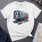 White t-shirt with a colorful train graphic and 'New York' text on a gray surface with a map and denim jacket.