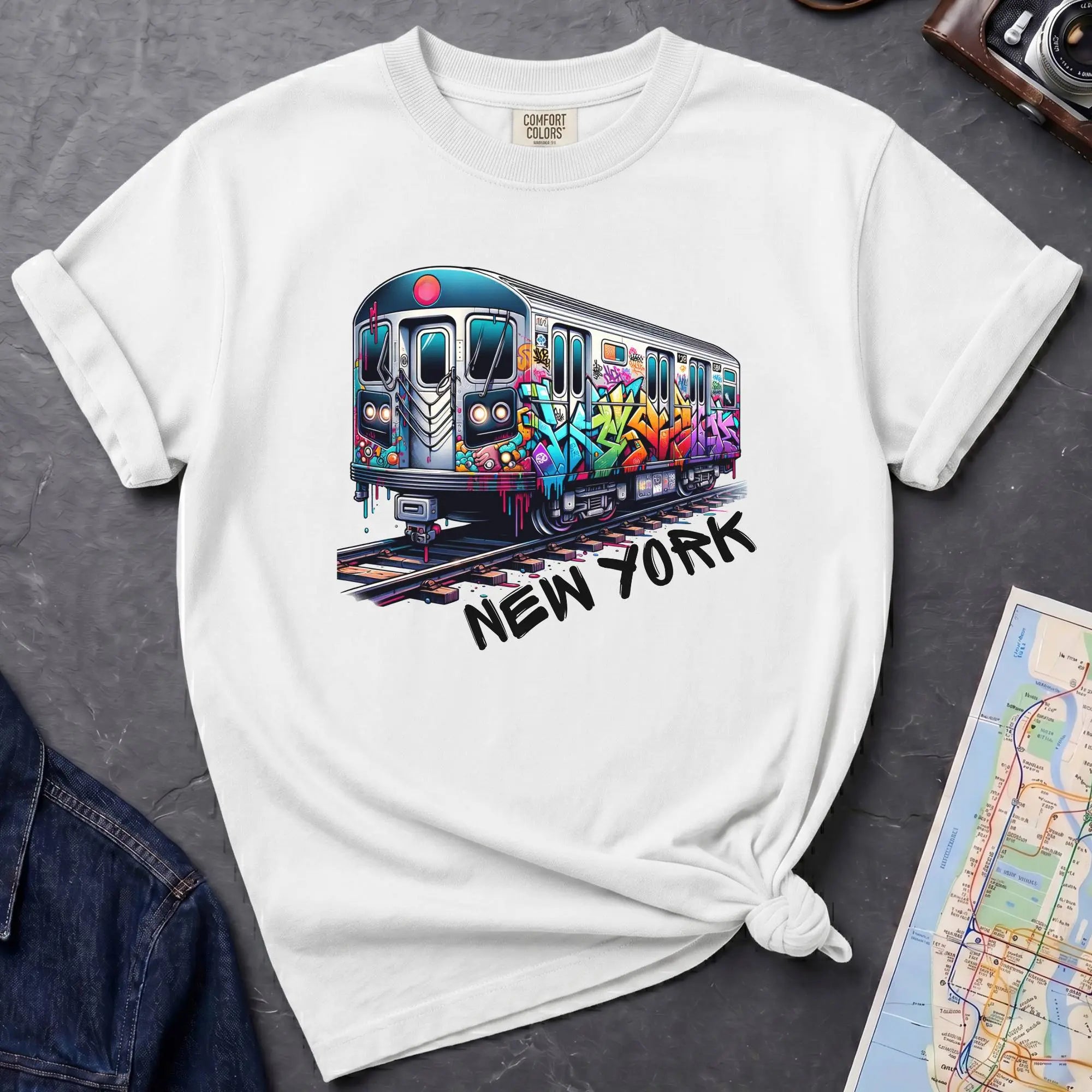 White t-shirt with a colorful train graphic and 'New York' text on a gray surface with a map and denim jacket.