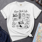 White t-shirt with New York-themed graphics on a gray surface with a map and camera.