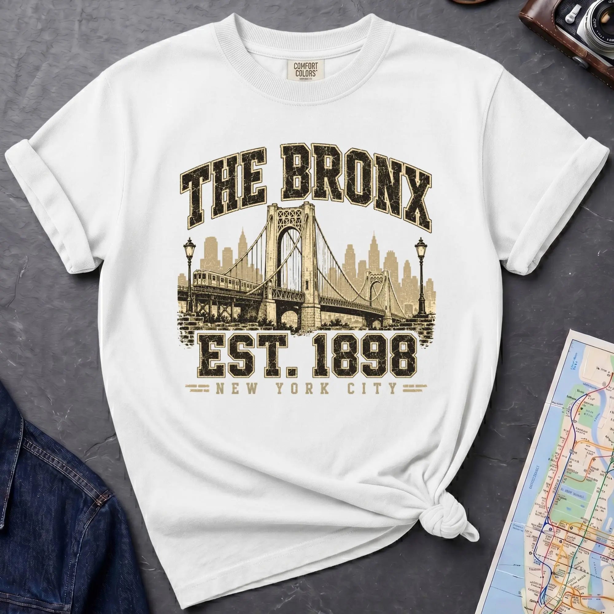 White t-shirt with 'The Bronx Est. 1898' design on a gray surface with a map and jacket.