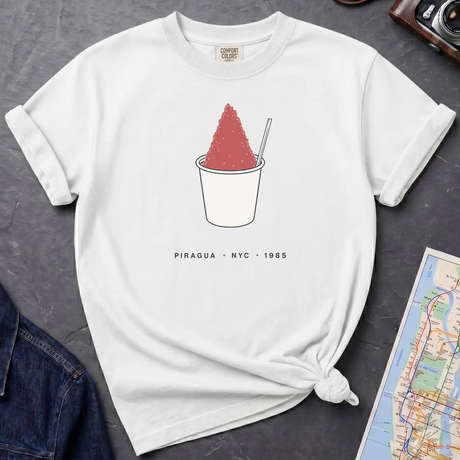 White Comfort Colors t-shirt with a piragua graphic and text, placed on a dark surface with a map and denim jacket.