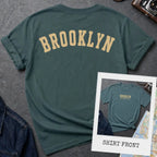 Blue Spruce colored Comfort Colors t-shirt with 'Brooklyn' printed on the back and 'Brooklyn, New York City', on a dark surface. 