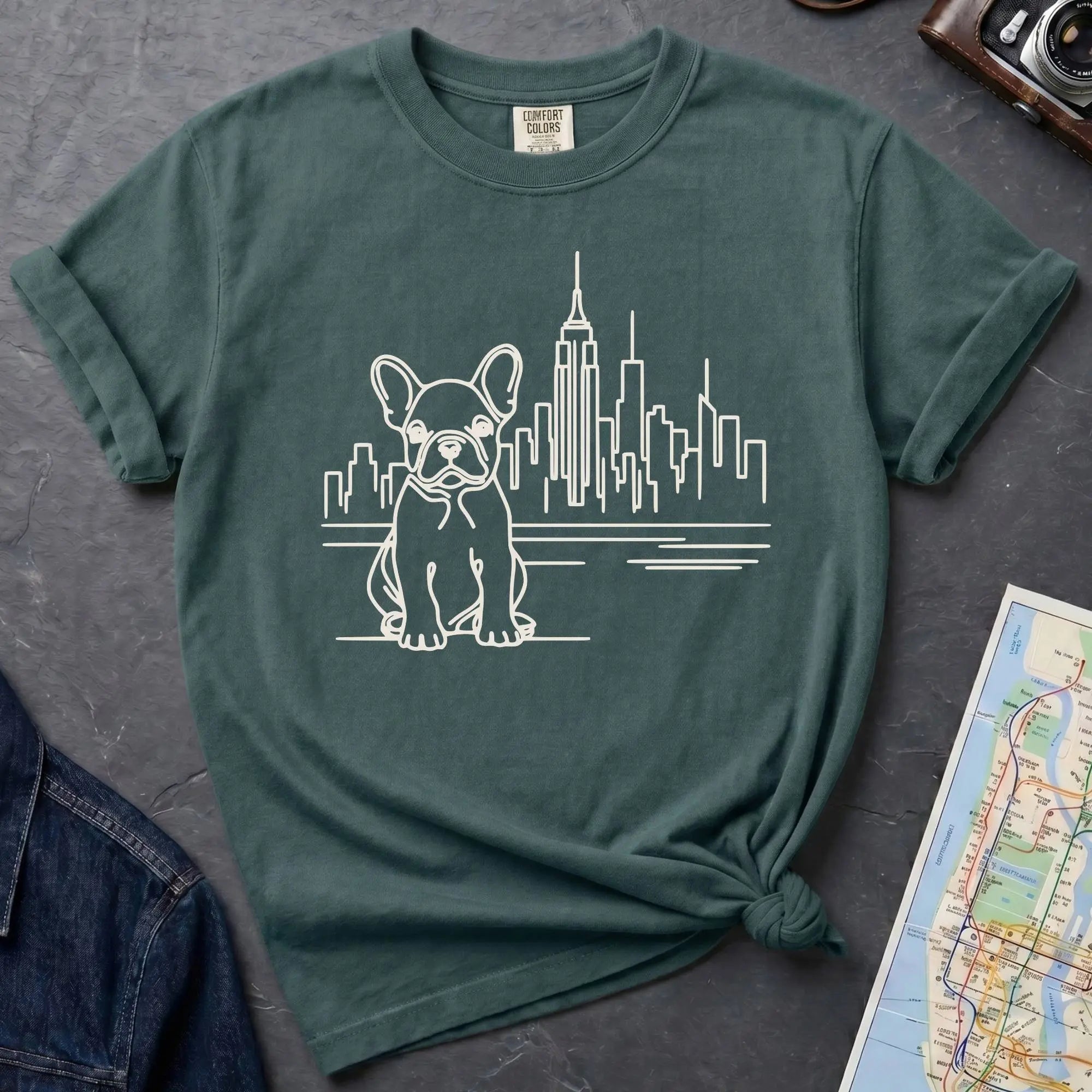 Blue spruce t-shirt with a French Bulldog and cityscape design on a gray surface with a denim jacket and a map.