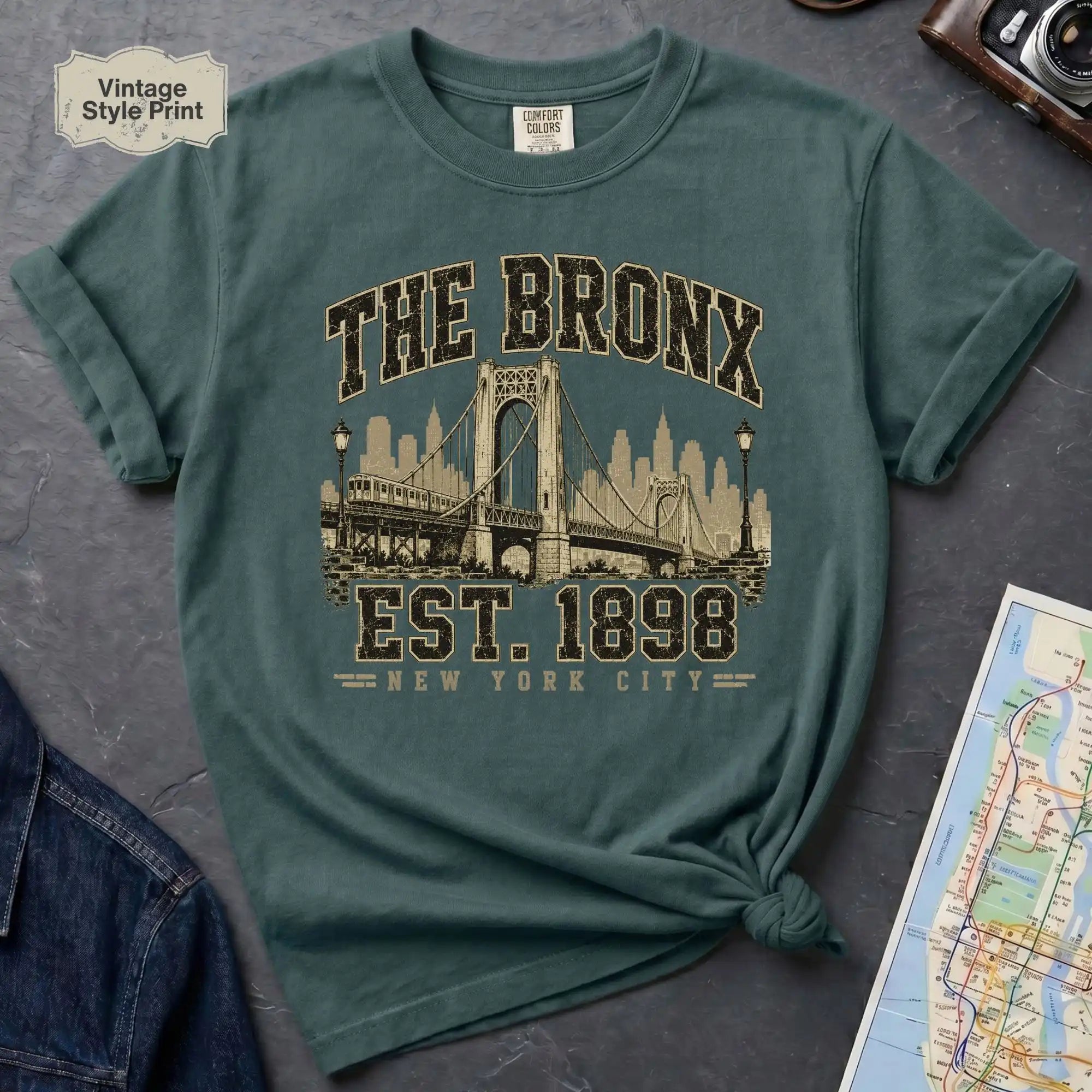 Blue Spruce colored t-shirt with 'The Bronx Est. 1898' print on a dark surface with a map and jeans.