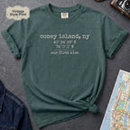 Blue Spruce t-shirt with text 'coney island, ny' and coordinates on a gray surface with a map and camera.