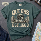Blue Spruce t-shirt with 'Queens Est. 1683' graphic design on a dark surface with a denim jacket and a map.