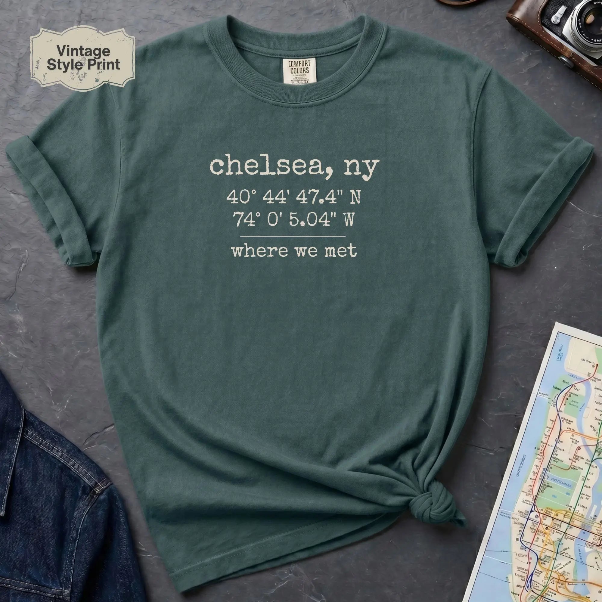 Green t-shirt with text 'chelsea, ny' and coordinates on a gray surface with a map and camera.