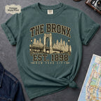 Blue spruce t-shirt with 'The Bronx Est. 1898' design on a dark surface with a map and a denim jacket.
