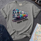 Granite colored t-shirt with a colorful train graphic and 'New York' text on a gray surface with a map and denim jacket.