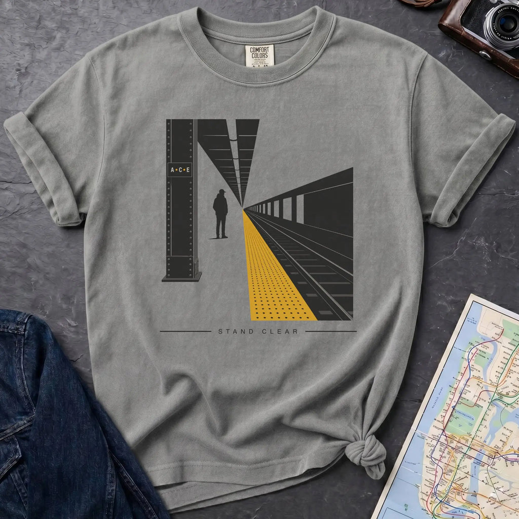 Granite colored t-shirt with a graphic design of a train station platform, denim jacket, and map on a dark surface