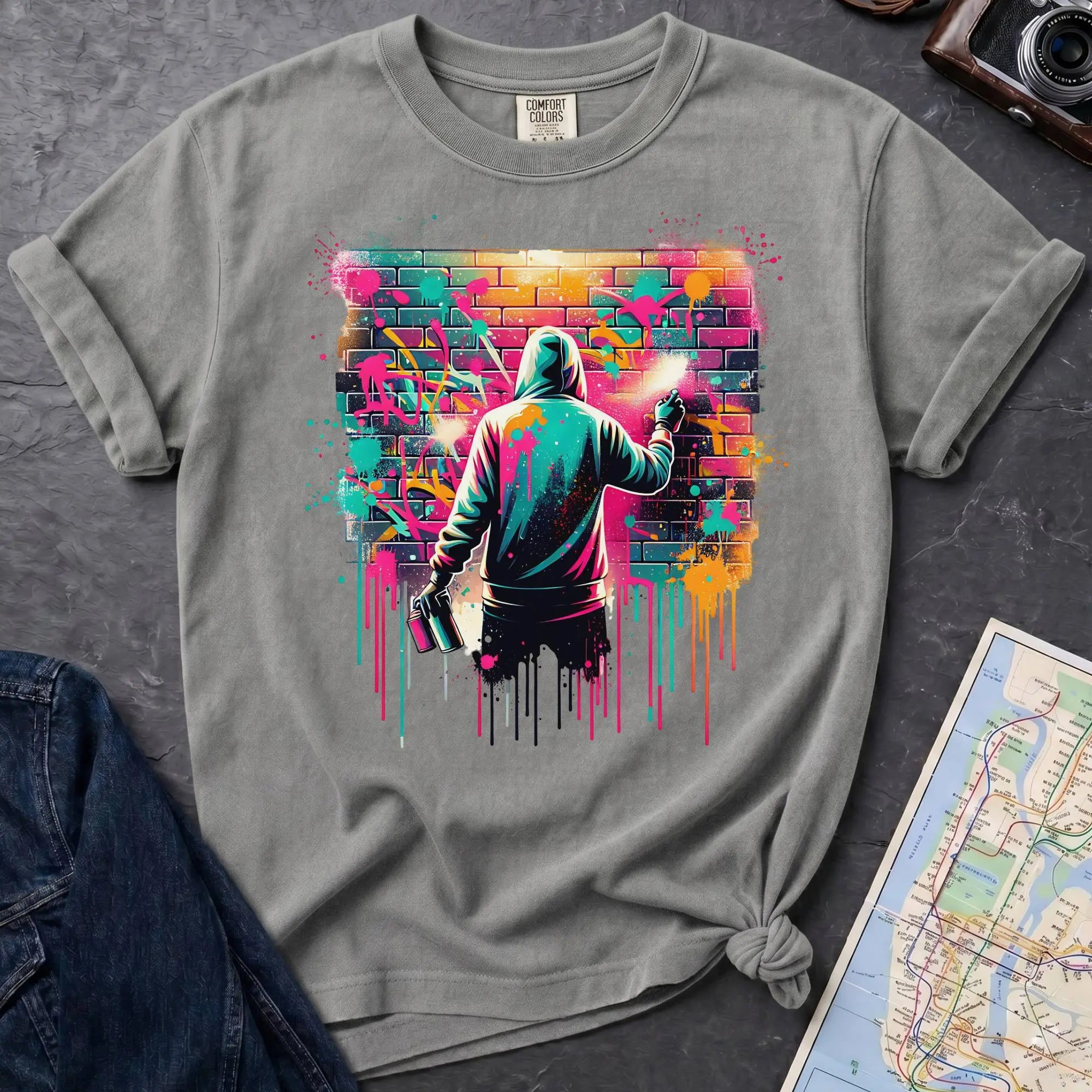 Granite colored t-shirt with a graphic of a person spray painting a colorful mural on a brick wall.