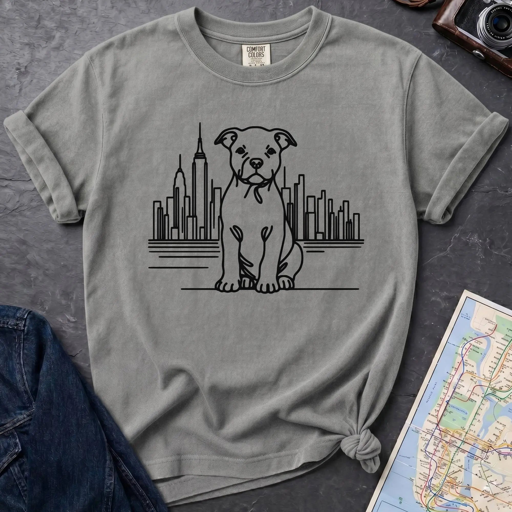 Granite colored t-shirt with a Pitbull dog and cityscape design on a dark surface with jeans and a map.