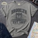 Granite colored Vintage-style Brooklyn NYC graphic t-shirt on a Bay colored Comfort Colors cotton shirt, featuring the Brooklyn Bridge and “Brooklyn Est. 1883” text.