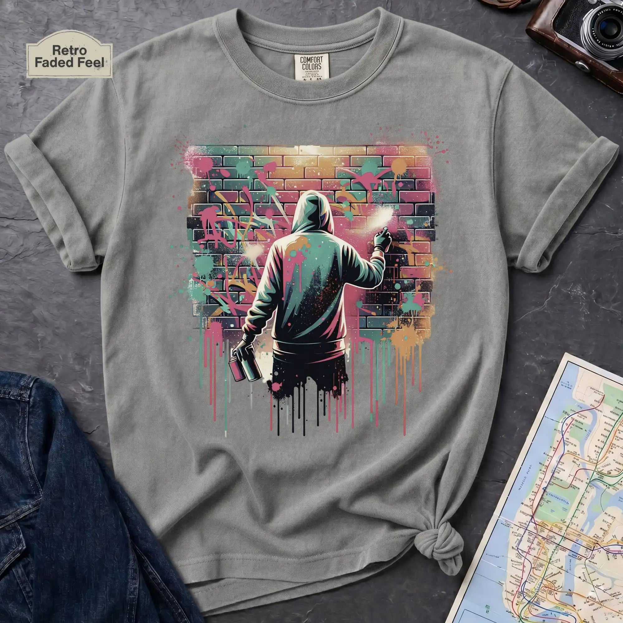 Gray t-shirt with a graphic of a person spray painting a colorful wall on a dark surface.