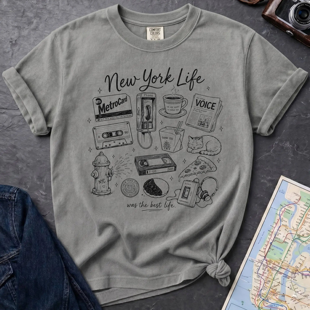 Granite colored t-shirt with New York-themed graphics on a gray surface with a map and camera.