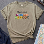 Khaki colored t-shirt with 'Queens' and NYC subway lines on a dark surface with a map and denim jacket.