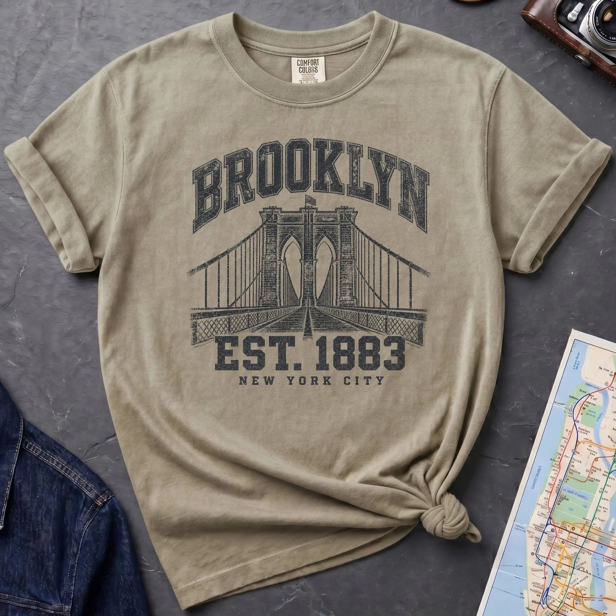 Khaki colored Vintage-style Brooklyn NYC graphic t-shirt on a Bay colored Comfort Colors cotton shirt, featuring the Brooklyn Bridge and “Brooklyn Est. 1883” text.