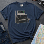 Navy blue t-shirt with a graphic design of a train seat and station sign on a dark surface with jeans and a map.