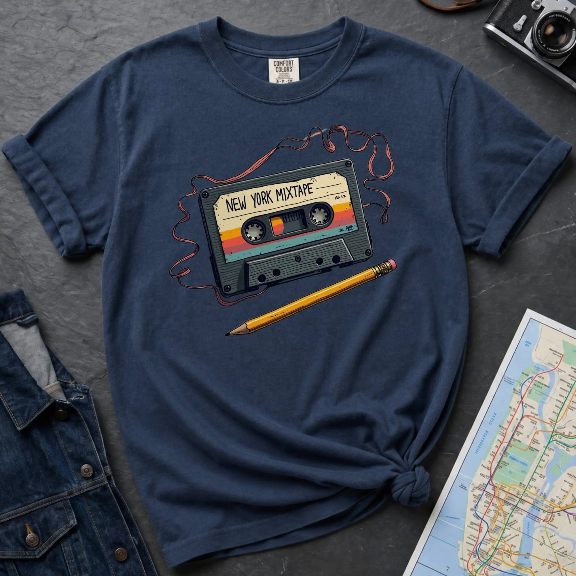 Navy t-shirt with a cassette tape graphic and pencil on a gray surface with denim jacket and map.