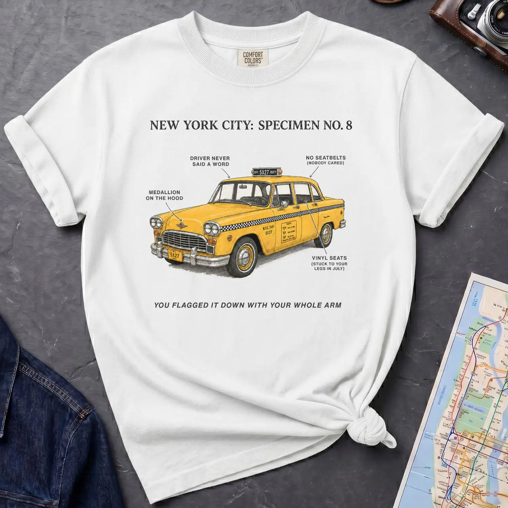 White Comfort Colors t-shirt with yellow taxi graphic and text on a dark surface with denim jacket and map.