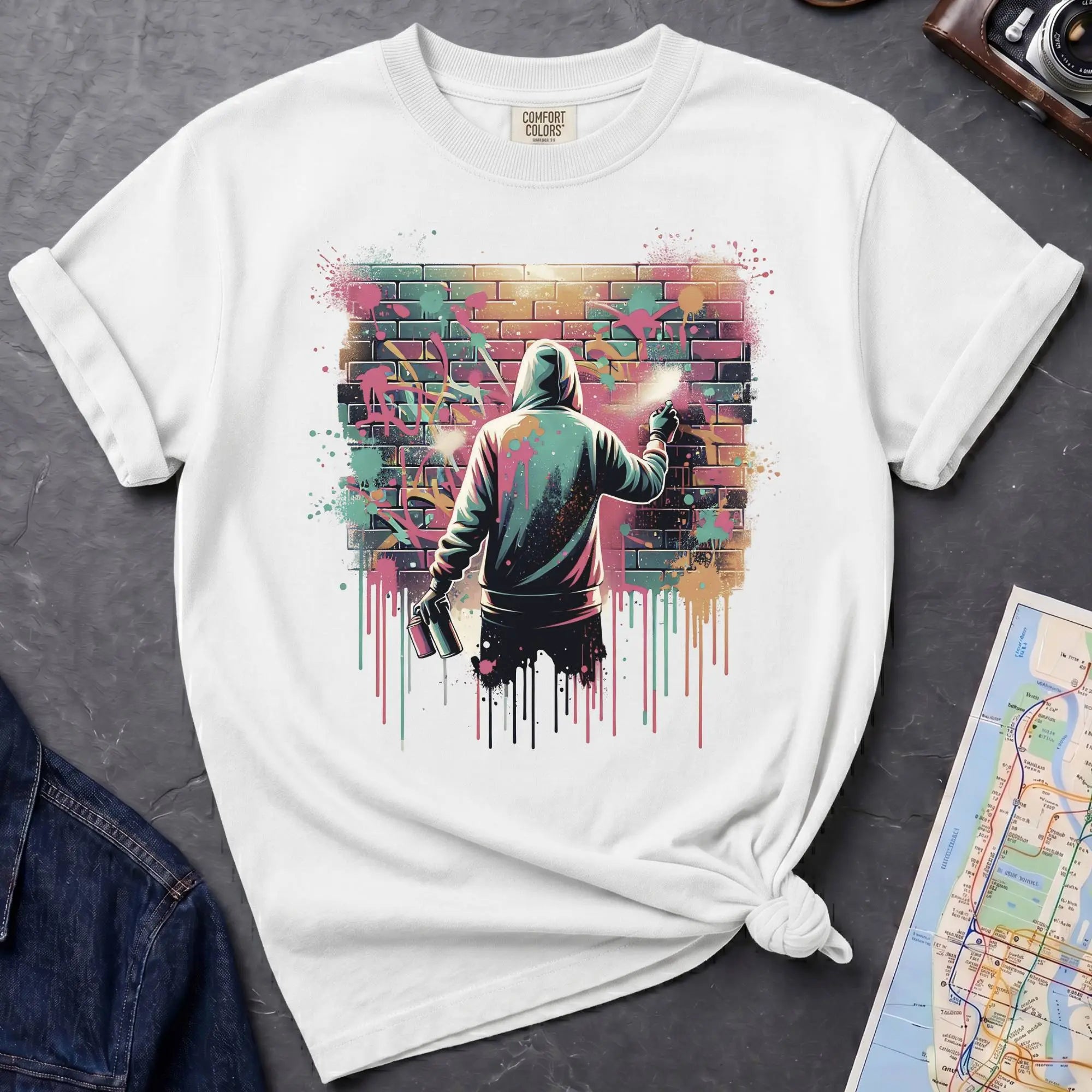 White t-shirt with a graphic of a person spray painting a colorful mural on a brick wall.