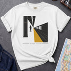 White t-shirt with a graphic design of a train station platform, denim jacket, and map on a dark surface