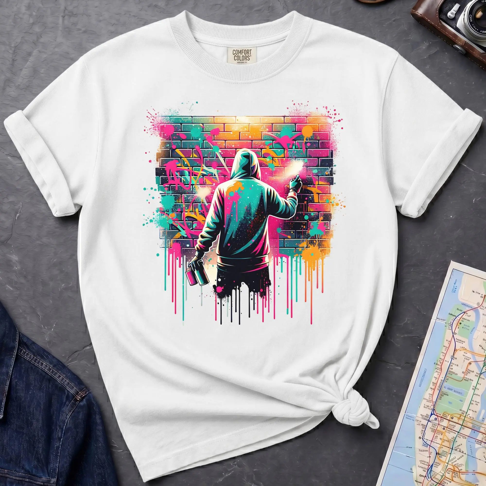 White t-shirt with a graphic of a person spray painting a colorful mural on a brick wall.