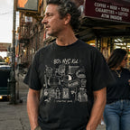 Man wearing a Black Comfort Colors t-shirt with an 80’s NYC Kid starter pack graphic featuring Italian ice, stickball, a fire hydrant, corner coffee, and stoop illustrations.