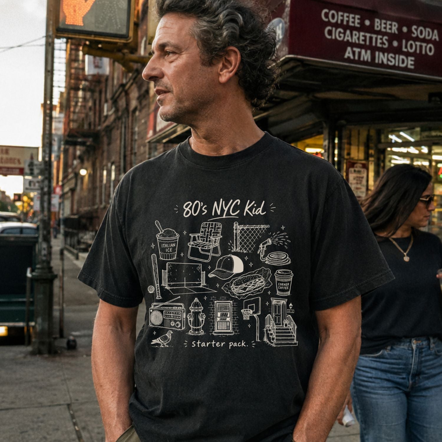 Man wearing a Black Comfort Colors t-shirt with an 80’s NYC Kid starter pack graphic featuring Italian ice, stickball, a fire hydrant, corner coffee, and stoop illustrations.