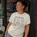 Woman wearing a '80s NYC Subway Survival Kit' t-shirt standing in front of a store with neon signs.