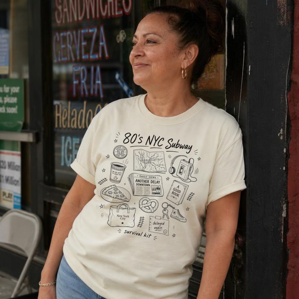 Woman wearing a '80s NYC Subway Survival Kit' t-shirt standing in front of a store with neon signs.