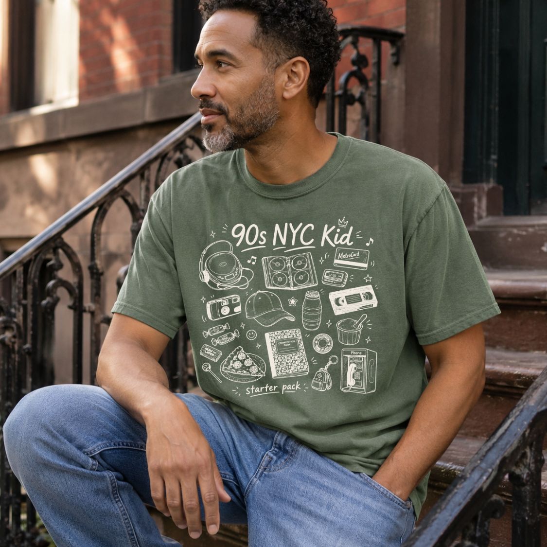 Man wearing a Moss colored Comfort Colors t-shirt with '90s NYC Kid' design sitting on steps.