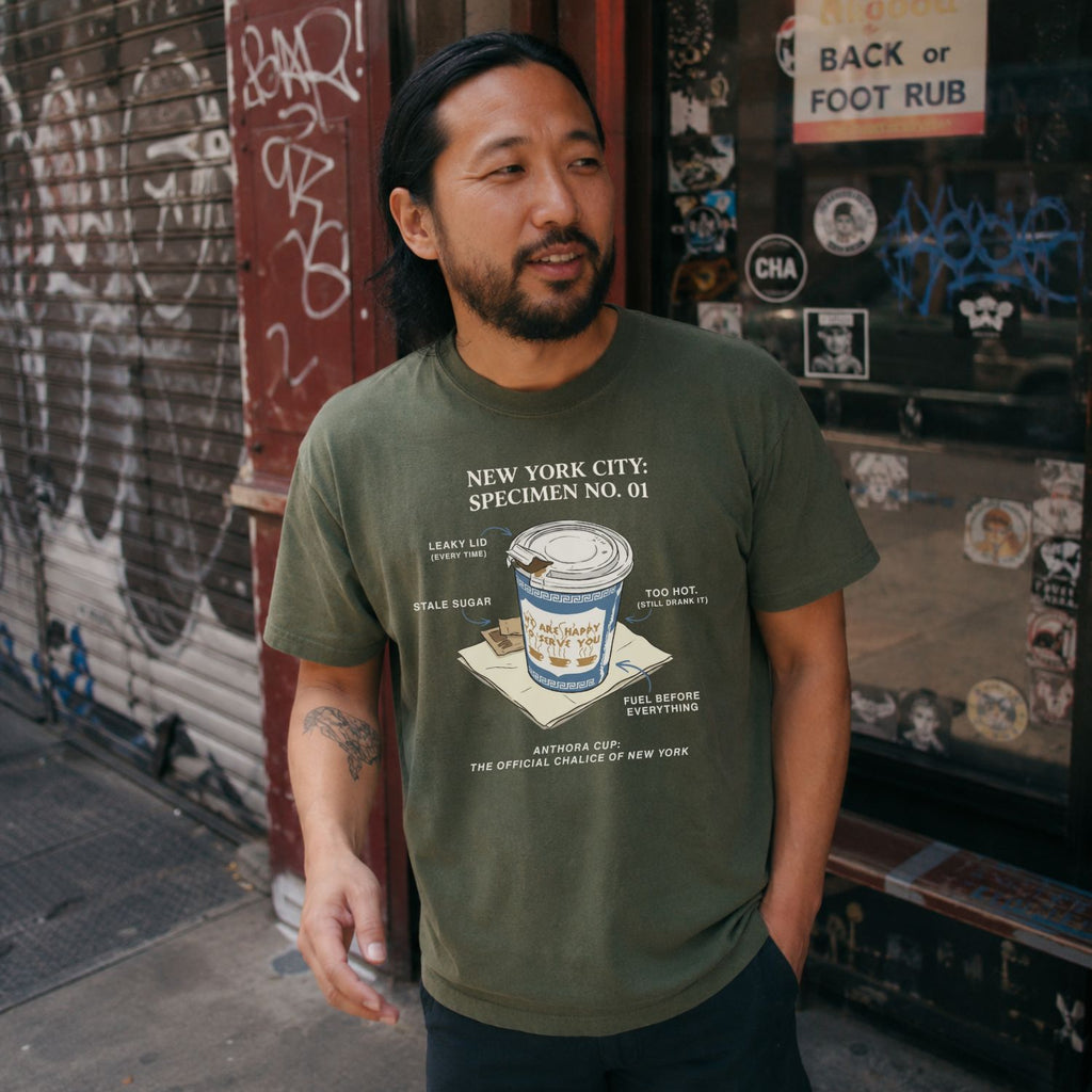 A man wearing a Moss green t-shirt with New York City coffee cup graphic.