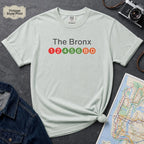 Light blue t-shirt with 'The Bronx' and subway line numbers printed on it, placed on a dark surface with a map and denim jacket.