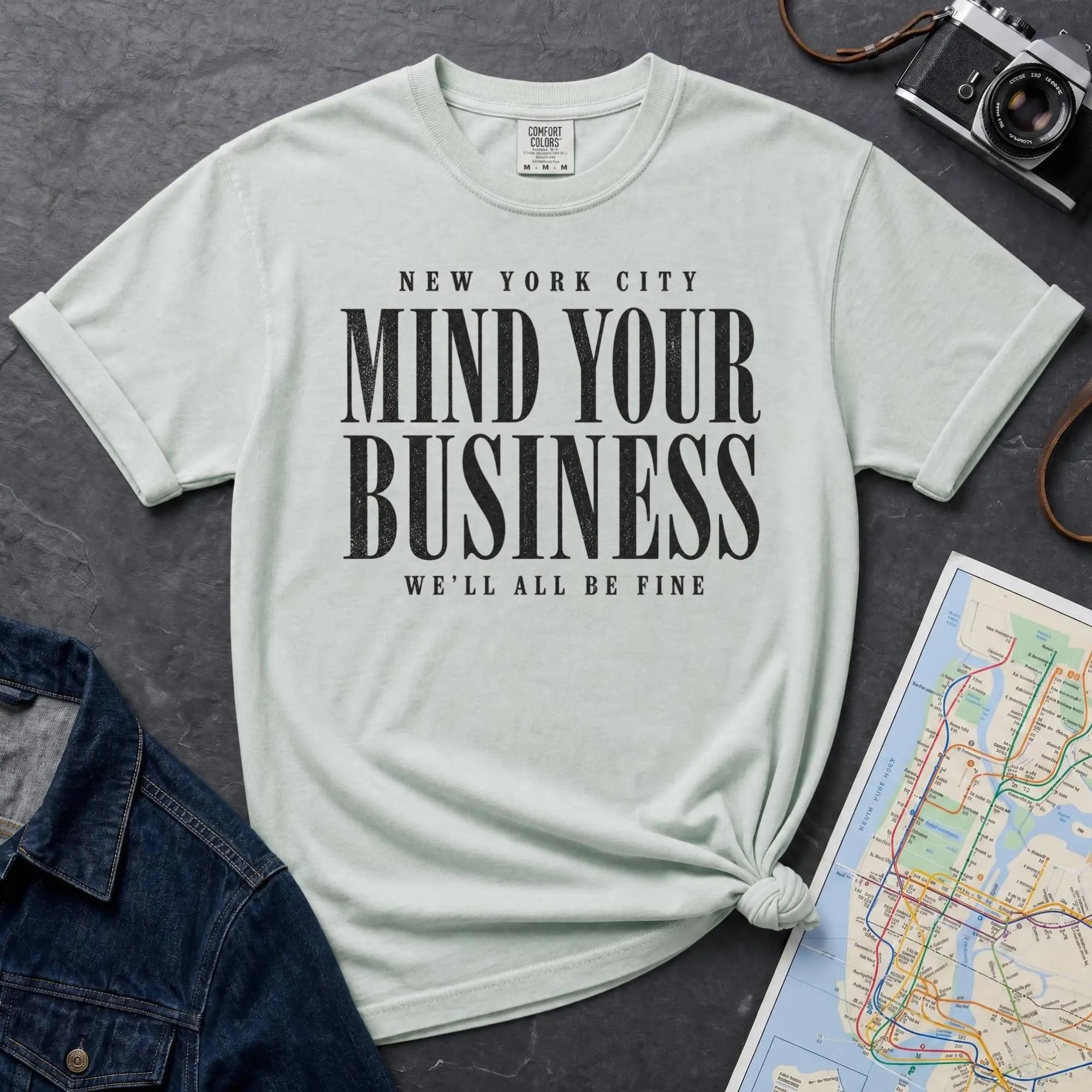 Bay colored Comfort Colors t-shirt featuring bold New York City “Mind Your Business, We’ll All Be Fine” text in a vintage black typography design.