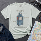 Bay colored t-shirt with a newspaper box graphic and text on a textured surface with a camera and map.