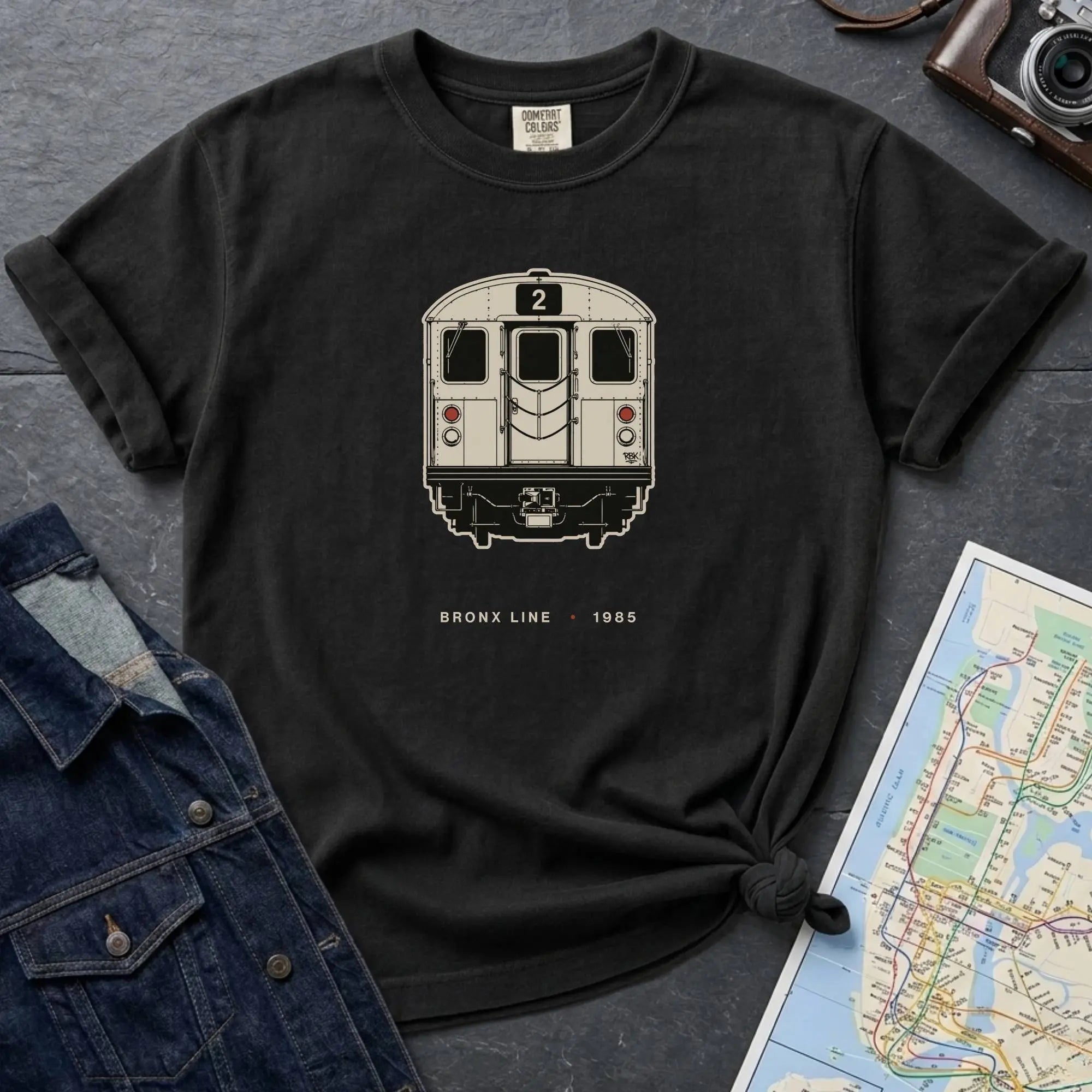 Black t-shirt with a NYC subway train graphic on a dark surface with a map and a denim jacket.