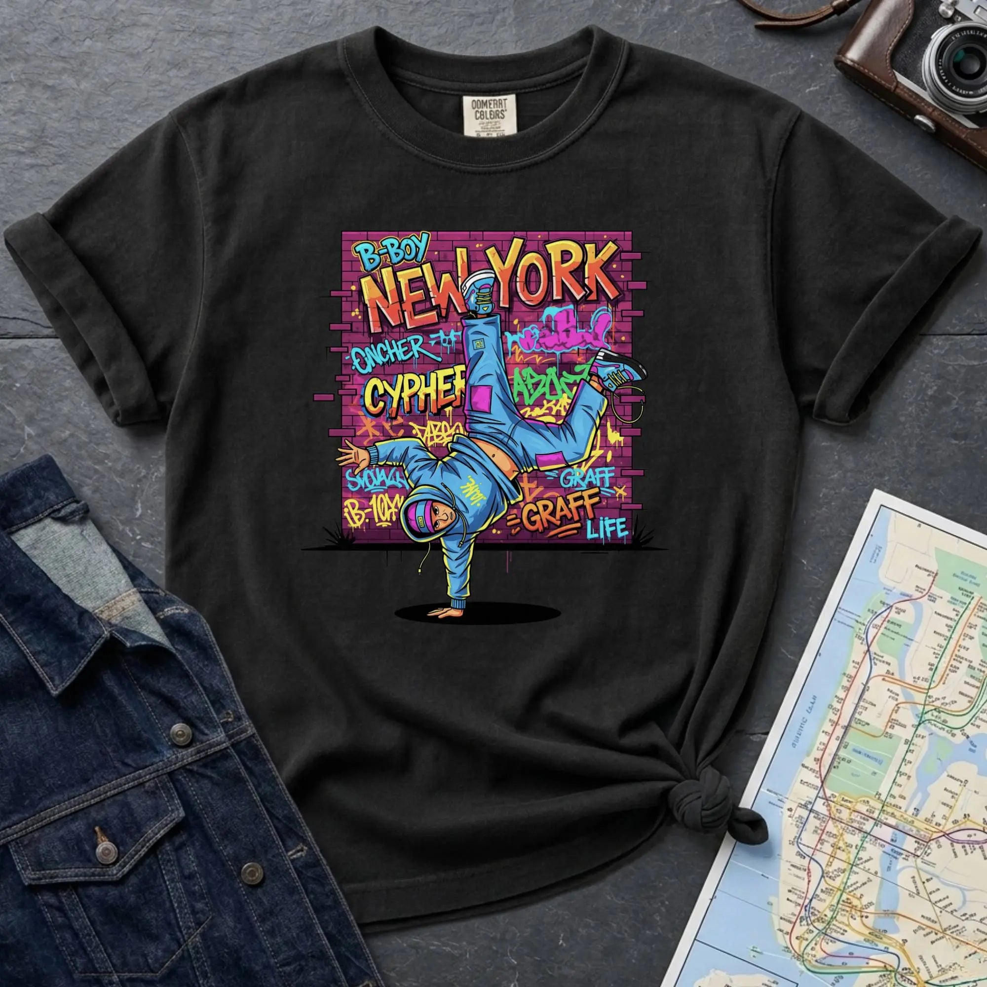 Black Comfort Colors t-shirt featuring a colorful B-Boy New York graphic with a breakdancer in front of a graffiti brick wall.