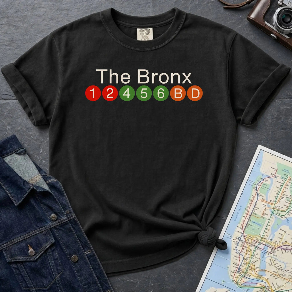 Black Comfort Colors t-shirt featuring a minimalist Bronx subway line graphic with The Bronx text and colorful NYC train icons.