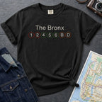 Black t-shirt with 'The Bronx' and subway line numbers on a dark surface with a map and camera.