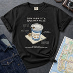 Black t-shirt with New York City coffee cup graphic on a textured surface with map and camera.