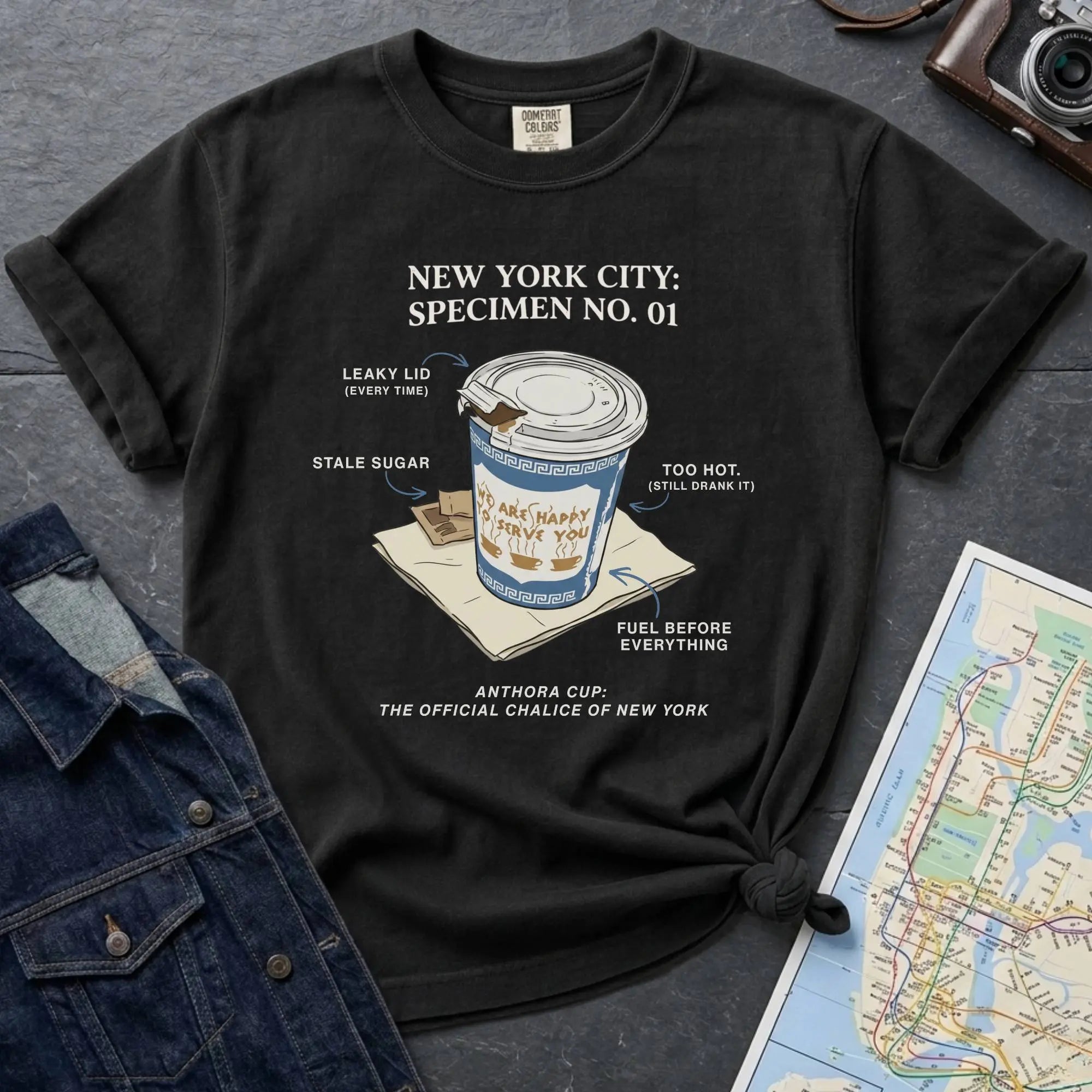 Black t-shirt with New York City coffee cup graphic on a textured surface with map and camera.