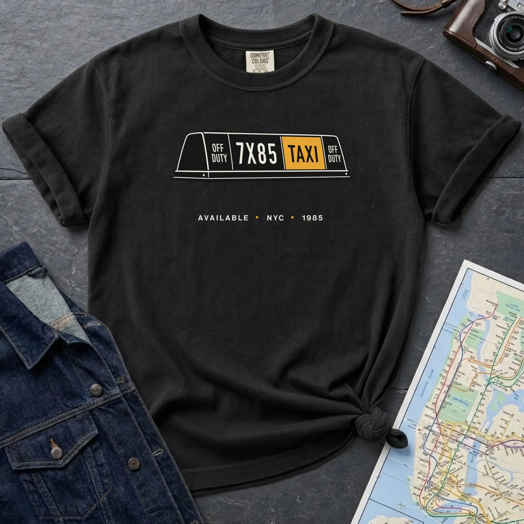 Black Comfort Colors t-shirt featuring a vintage New York City taxi roof sign graphic with “Available • NYC • 1985” text.